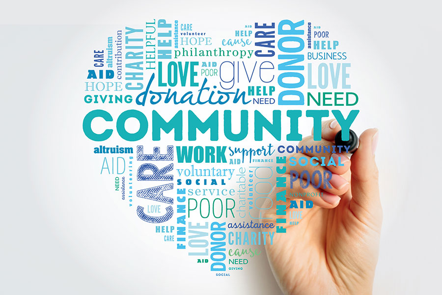 A hand holding a marker, drawing a word cloud in the shape of a heart. The words in the cloud include "Community," "Care," "Love," "Charity," "Donate," "Help," "Poor," "Give," and "Support," in varying sizes and colors, symbolizing the themes of giving, aid, and philanthropy.