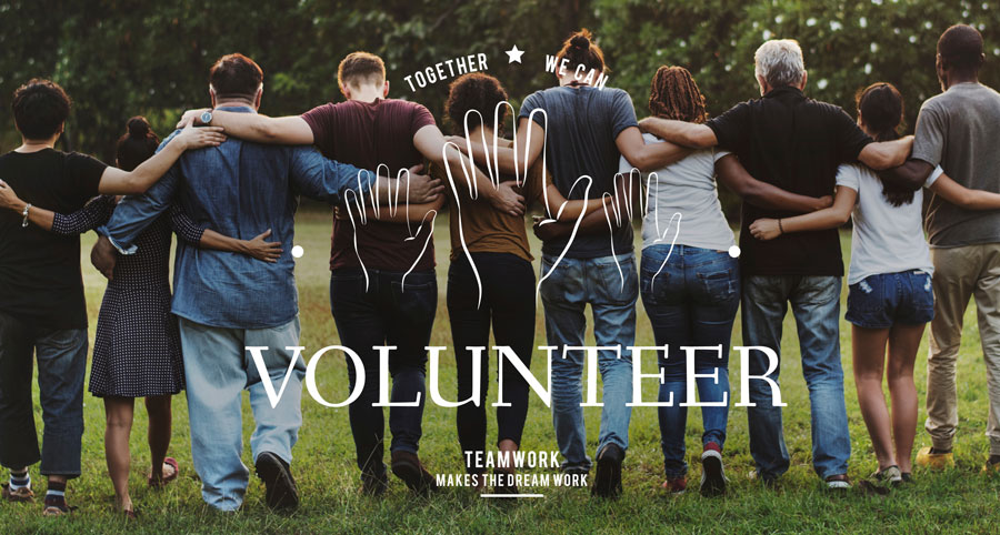 A diverse group of people standing together with their arms around each other, facing away from the camera. The word "VOLUNTEER" is written at the bottom with a slogan "TEAMWORK MAKES THE DREAM WORK" and hand illustrations above them. The background shows a grassy field with trees.
