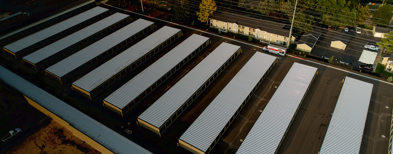 "An aerial view of a self-storage facility with multiple rows of storage units, showcasing the large, organized layout with a residential area in the background."