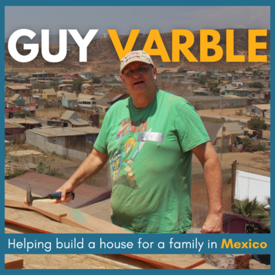Image of a man wearing a green t-shirt and a cap, holding a hammer while working on a construction site. The text 'GUY VARBLE' is prominently displayed, with a caption stating, 'Helping build a house for a family in Mexico.' The background shows a residential area in the distance.
