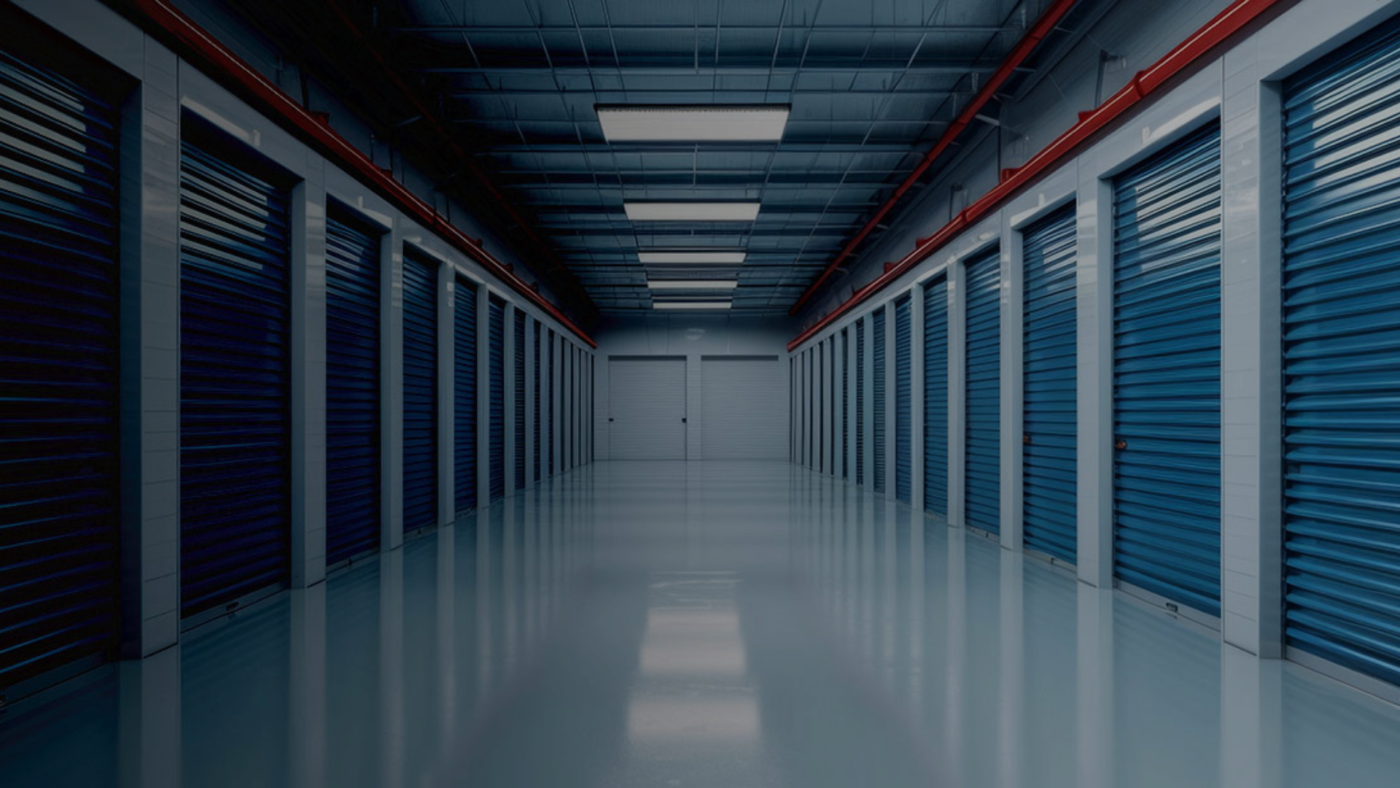 Interior view of a well-lit self-storage facility with several blue roll-up doors along a clean, polished floor, creating an organized and spacious corridor.