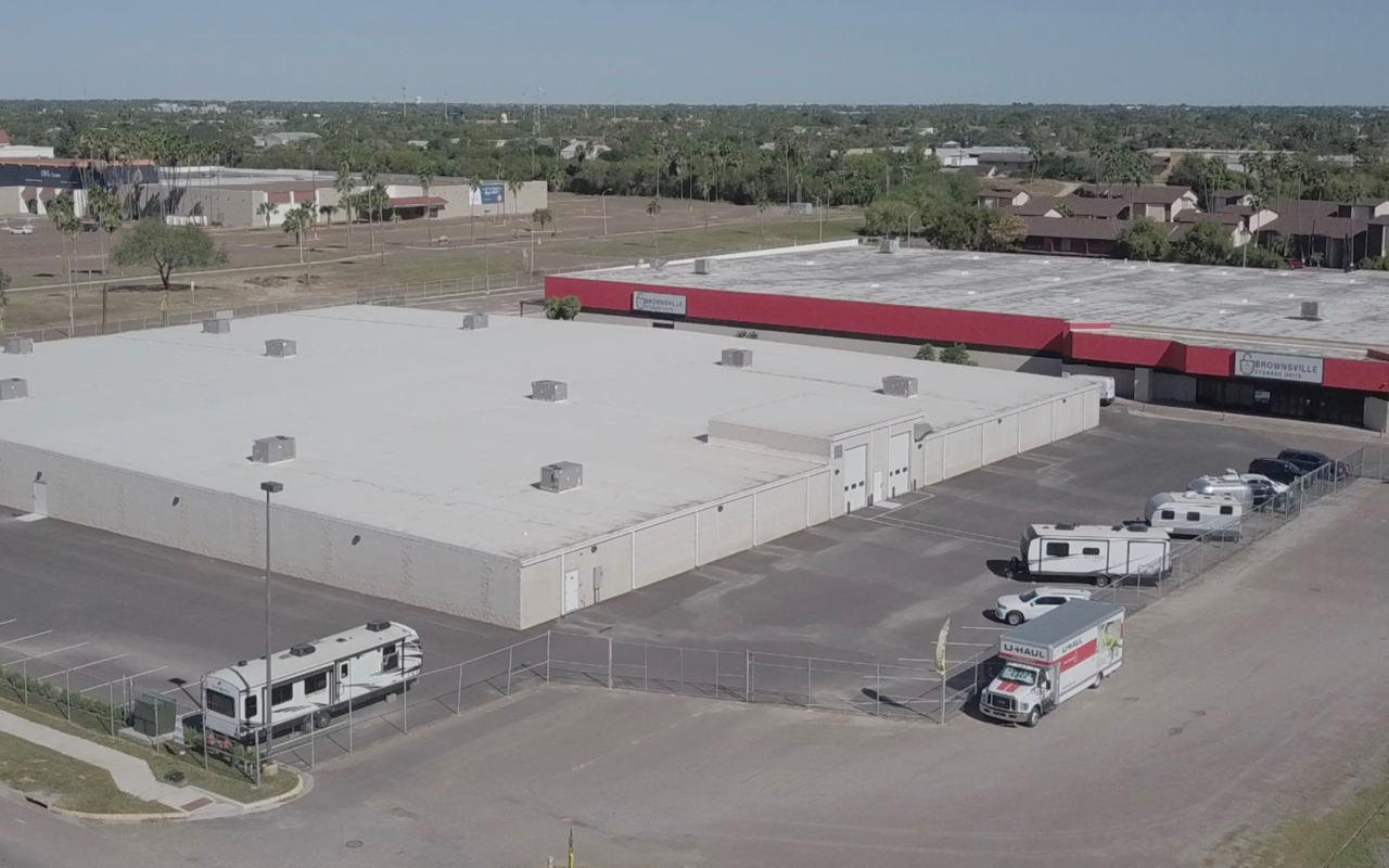 Aerial view of the Brownsville self-storage facility with white roofing, perimeter fencing, and vehicle storage including RVs and trailers.